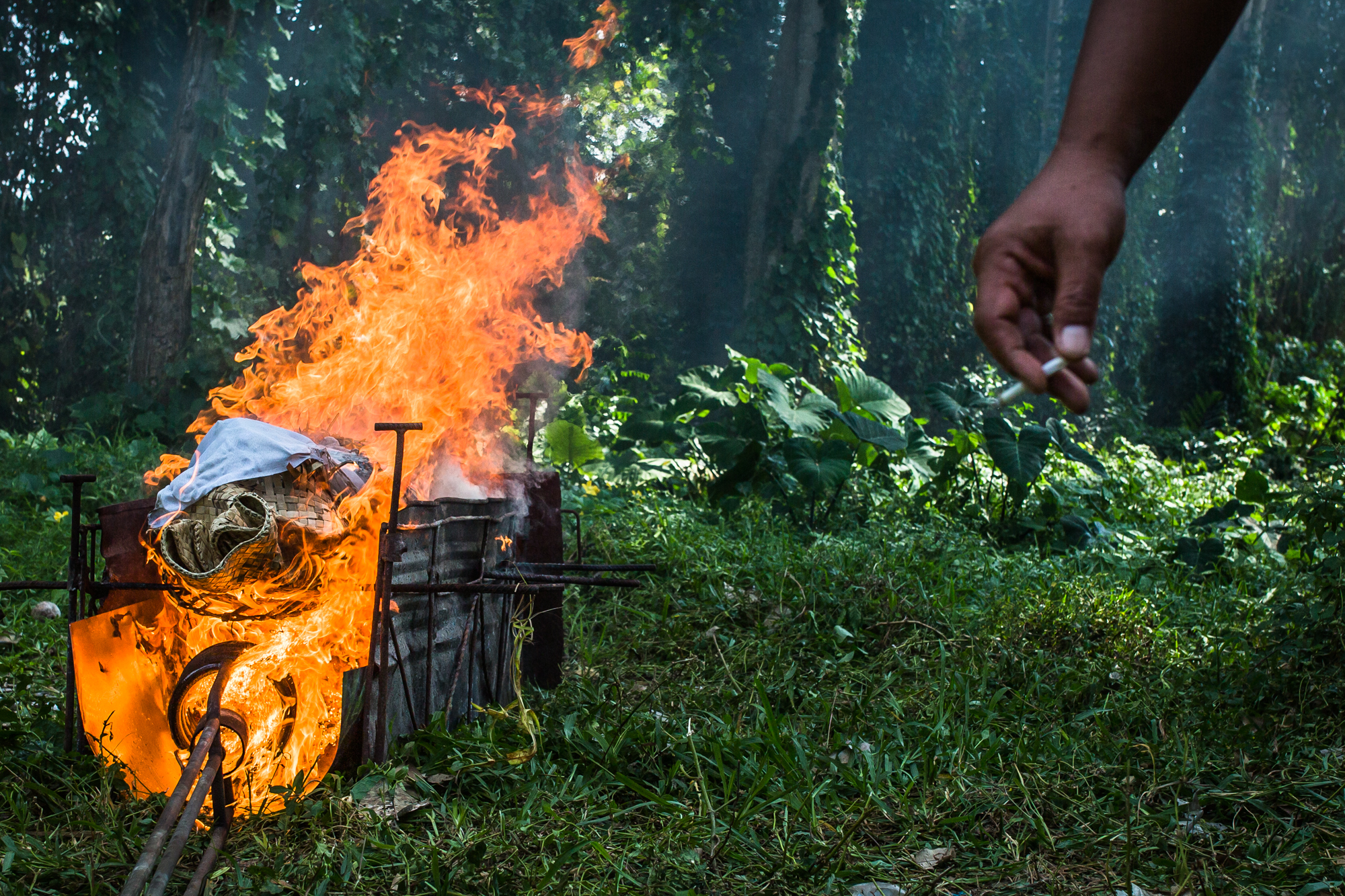 A man with a cigarette looks on as a cremation takes place in Bali, Indonesia