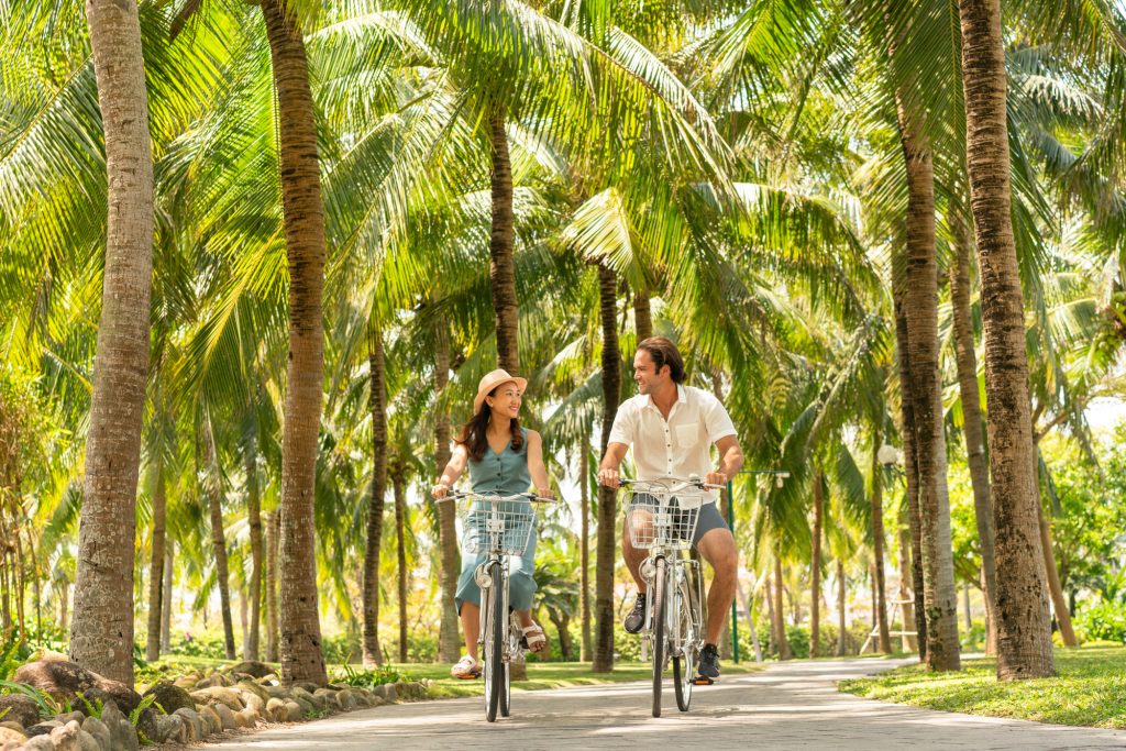 A couple ride bicycles through a lush garden at a luxury beach resort in Vietnam