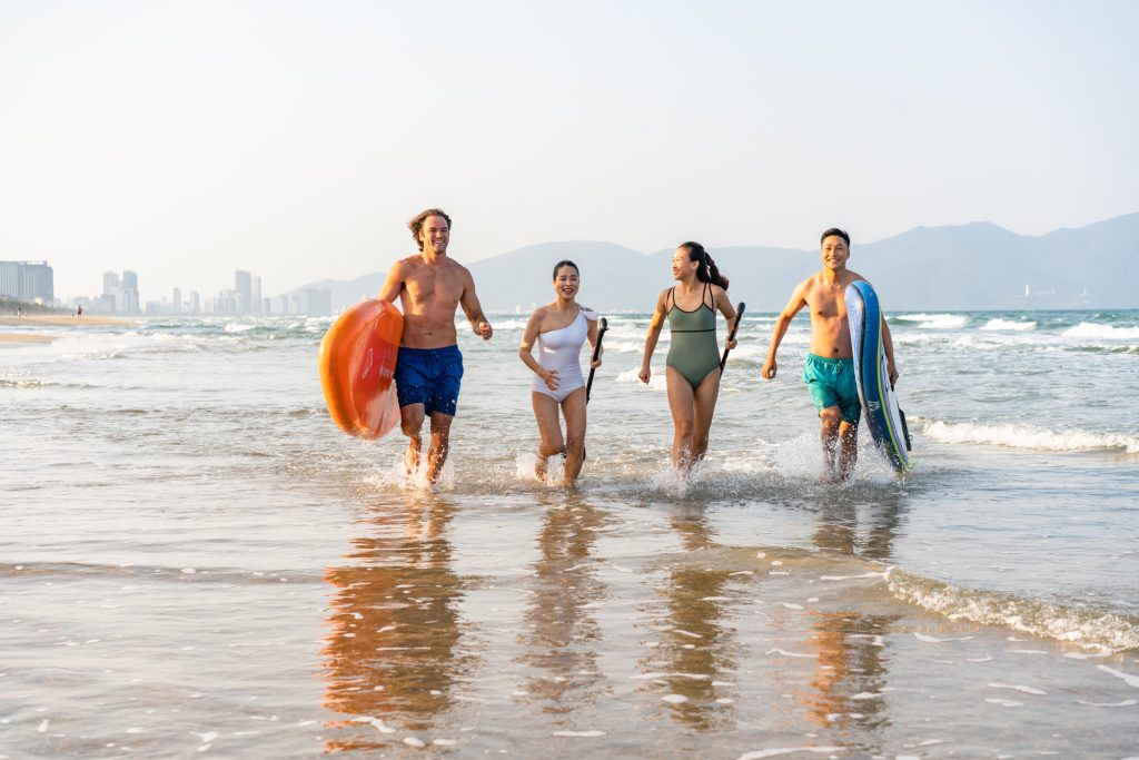 A group of friends run down the beach with stand up paddle boards in Vietnam