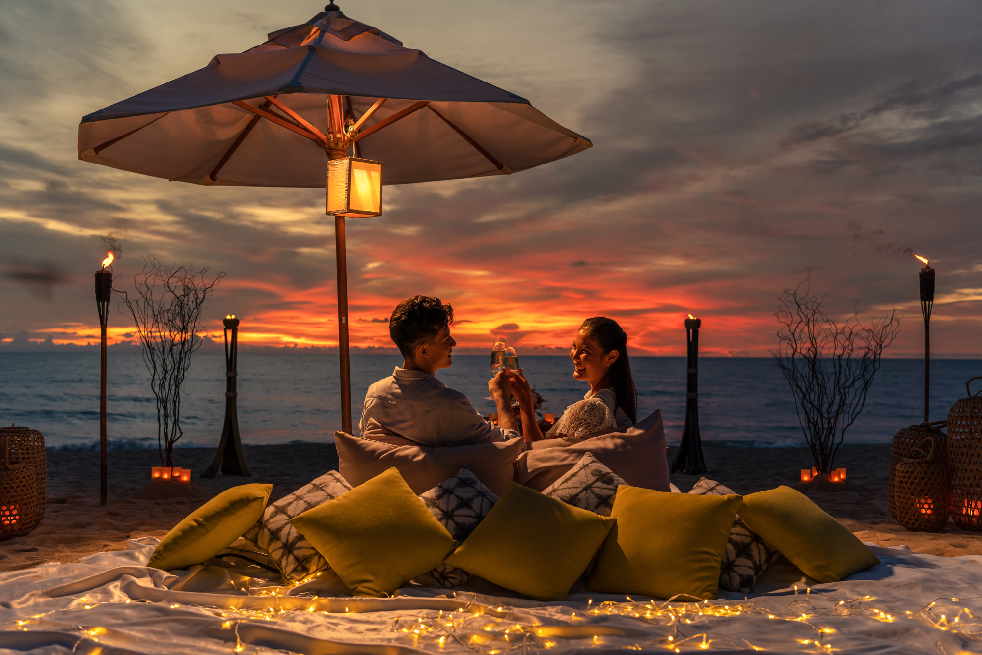 A couple enjoy a fiery sunset on the beach at a luxury resort in Thailand