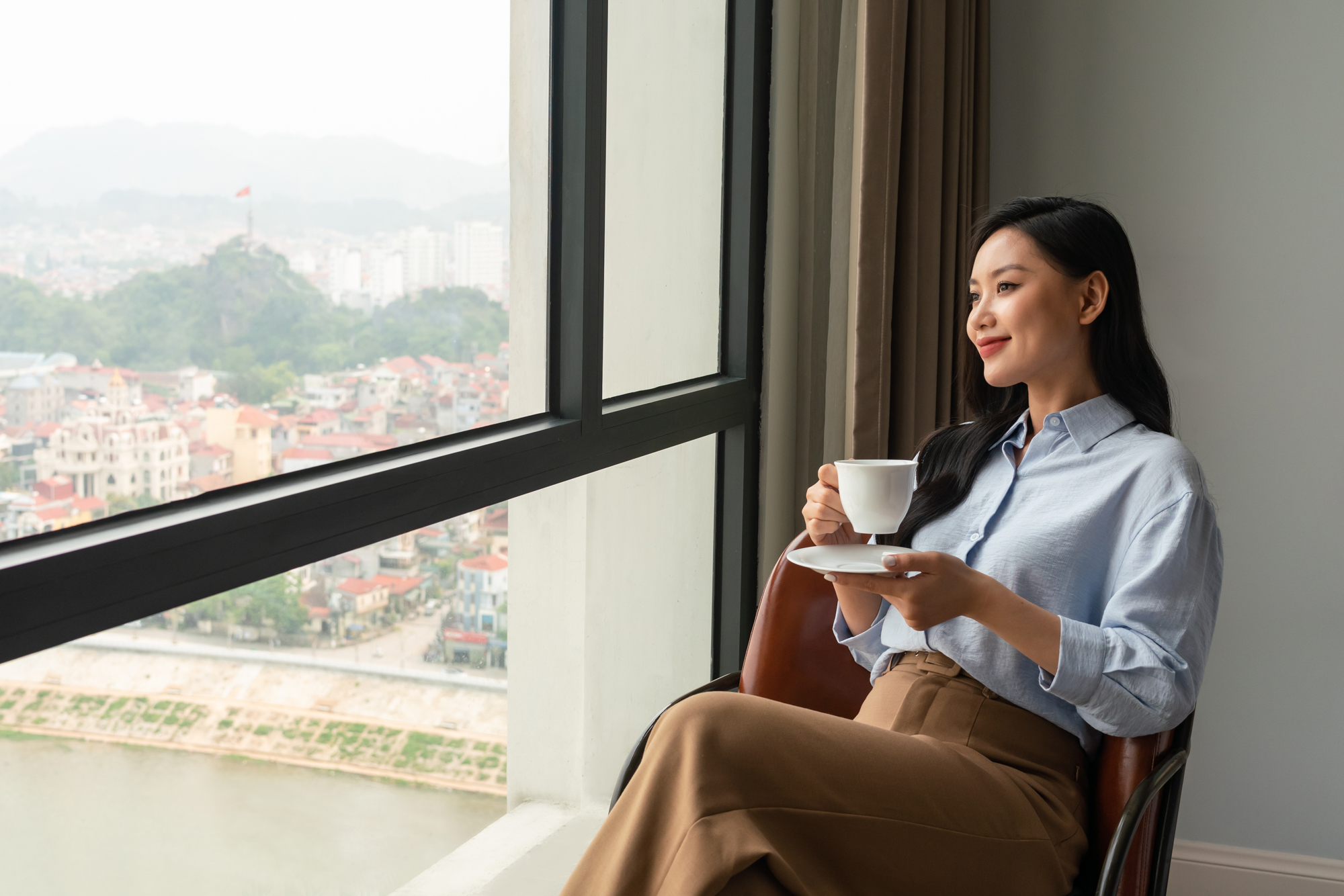 A woman enjoys a coffee and the views from her room in a five star hotel in Vietnam.
