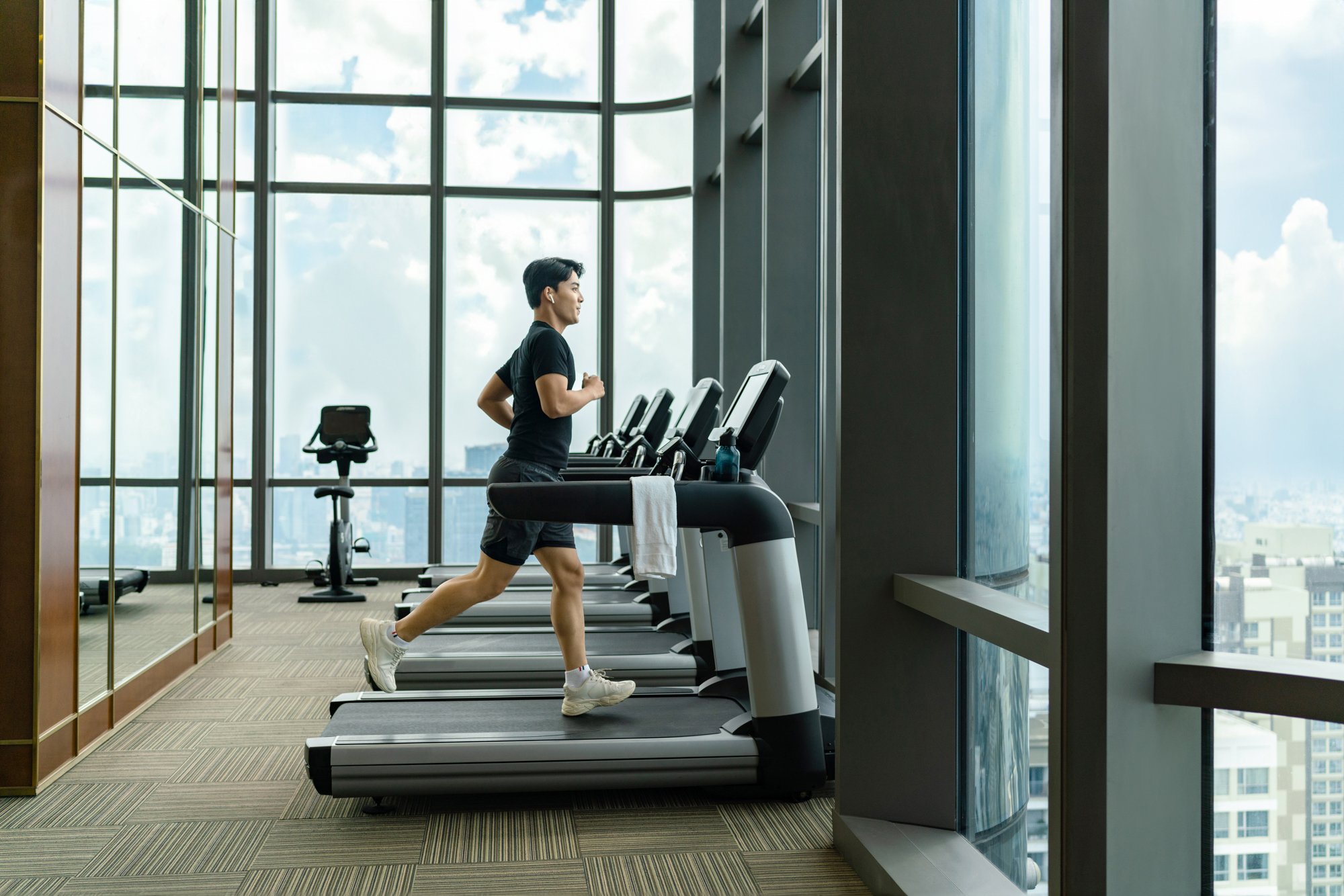A man runs on a treadmill at a hotel with large window views of the city below