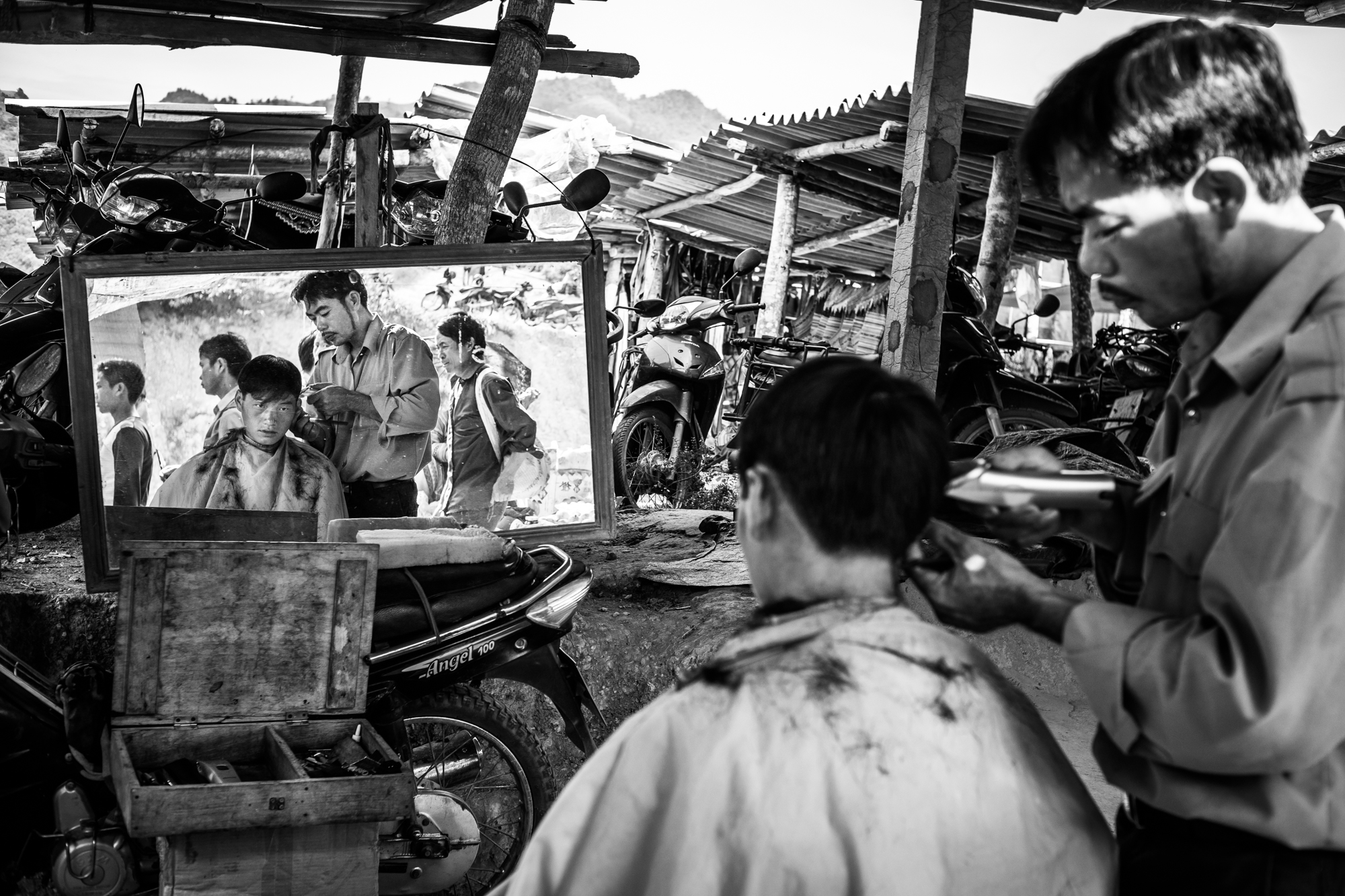 A man receives a haircut at a makeshift shop in Bac Ha market, Lao Cai Province, Vietnam. 2014